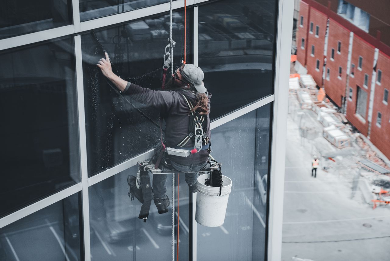 Un employé nettoyant les vitres d’un gratte-ciel avec un harnais dans un environnement urbain.