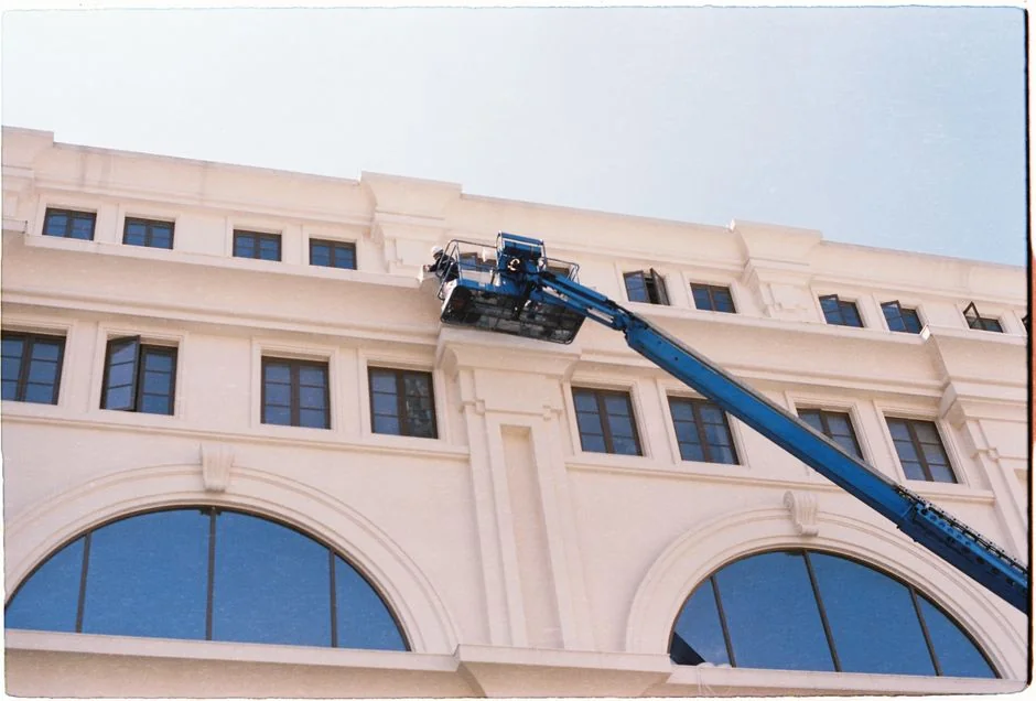 Un homme nettoie les vitres d'un gratte-ciel avec un harnais, illustrant le travail urbain en hauteur.